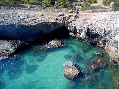 Torniamo cos� indietro e risaliamo la parete per affacciarci sulla costa rocciosa. Da qui su possiamo vedere la bocca della cavit�, che sbuca direttamente nel mare trasparente (foto di Pippo Vacca)